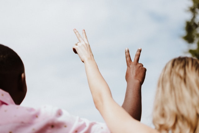 Two people, a black man and a white woman, holding their hands up in peace signs