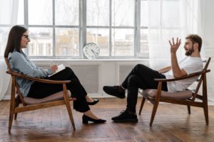 A man sits in a chair speaking to a therapist